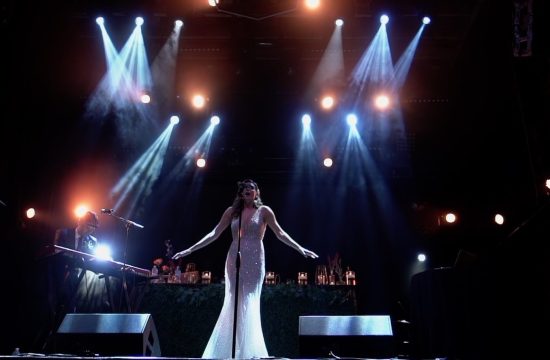 bride surrounded by stage lights singing in wedding dress with arms open